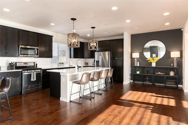 kitchen featuring a breakfast bar, hanging light fixtures, dark hardwood / wood-style flooring, an island with sink, and stainless steel appliances