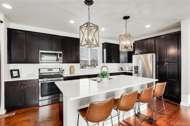 kitchen featuring appliances with stainless steel finishes, pendant lighting, an island with sink, sink, and a kitchen breakfast bar