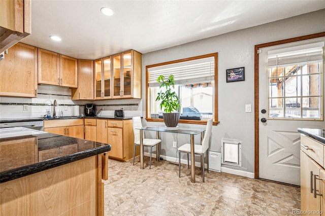 kitchen featuring glass insert cabinets, a healthy amount of sunlight, tasteful backsplash, and a sink