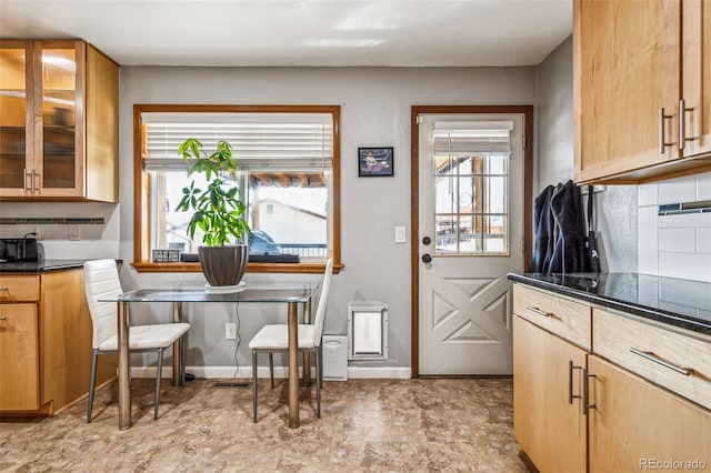 kitchen with backsplash, glass insert cabinets, baseboards, and dark countertops