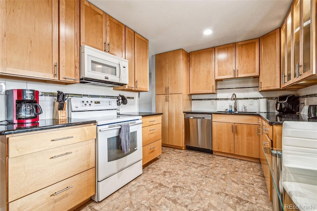 kitchen with dark countertops, glass insert cabinets, decorative backsplash, white appliances, and a sink