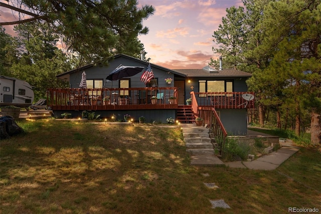 back house at dusk with a wooden deck and a yard