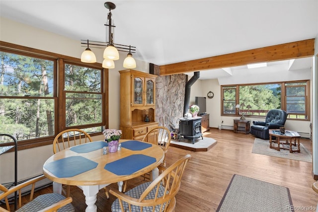 dining room featuring light wood-style floors, baseboard heating, a wood stove, and beam ceiling