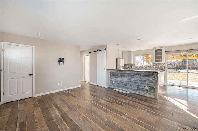 unfurnished living room featuring a barn door, baseboards, and wood finished floors