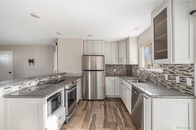 kitchen featuring stainless steel appliances, a peninsula, wood finished floors, a sink, and glass insert cabinets