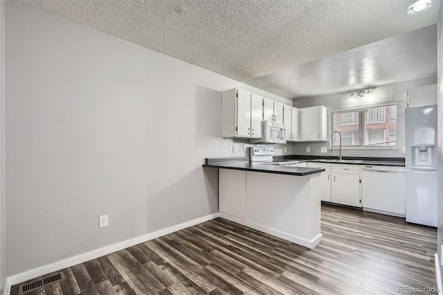 kitchen with visible vents, a peninsula, dark wood-style floors, white appliances, and a sink