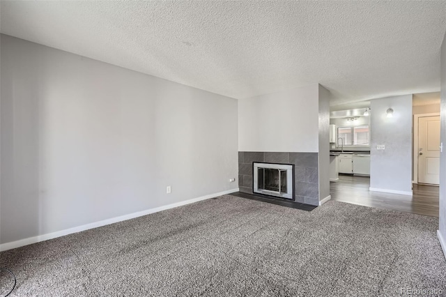 unfurnished living room featuring a tiled fireplace, sink, dark carpet, and a textured ceiling