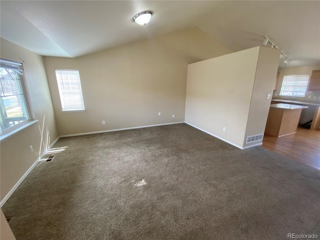 empty room with lofted ceiling, baseboards, visible vents, and dark carpet