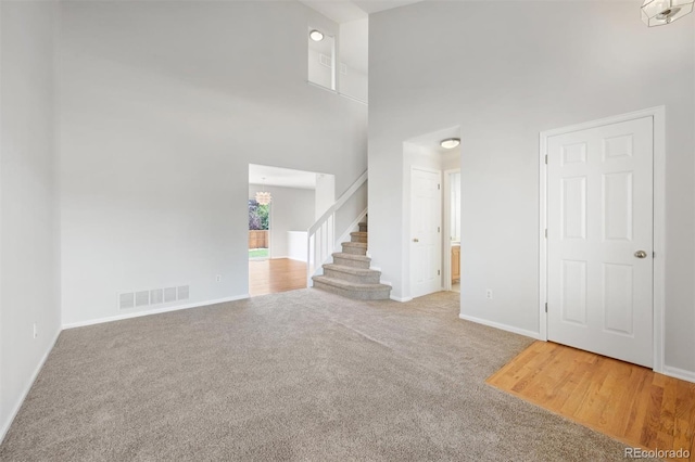 carpeted empty room with a towering ceiling and a notable chandelier