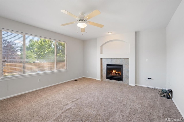 unfurnished living room with ceiling fan, carpet floors, and a tiled fireplace