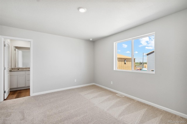 unfurnished bedroom featuring ensuite bathroom, visible vents, baseboards, and carpet floors