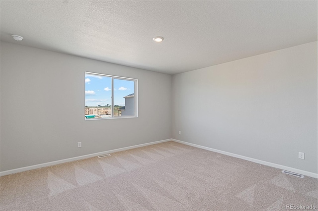 unfurnished room with light colored carpet, a textured ceiling, visible vents, and baseboards