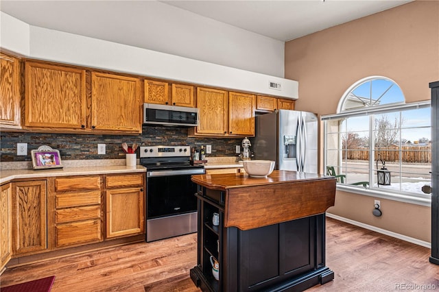 kitchen featuring a kitchen island, appliances with stainless steel finishes, light wood-type flooring, and decorative backsplash