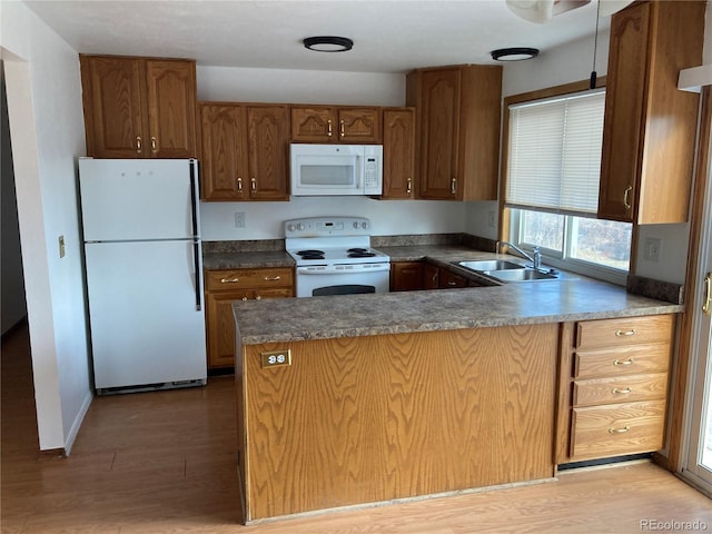 kitchen featuring light wood finished floors, a peninsula, white appliances, and a sink