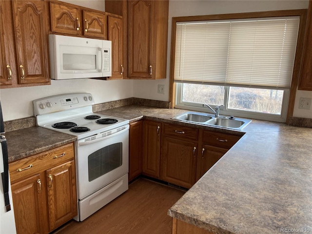 kitchen with white appliances, brown cabinetry, dark countertops, and a sink