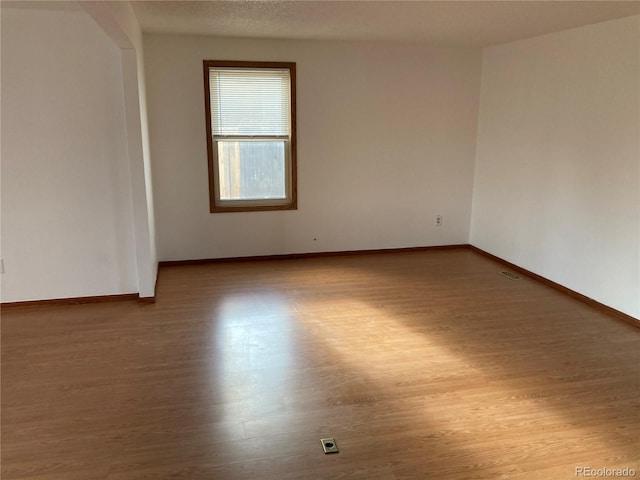 spare room featuring baseboards, a textured ceiling, visible vents, and wood finished floors