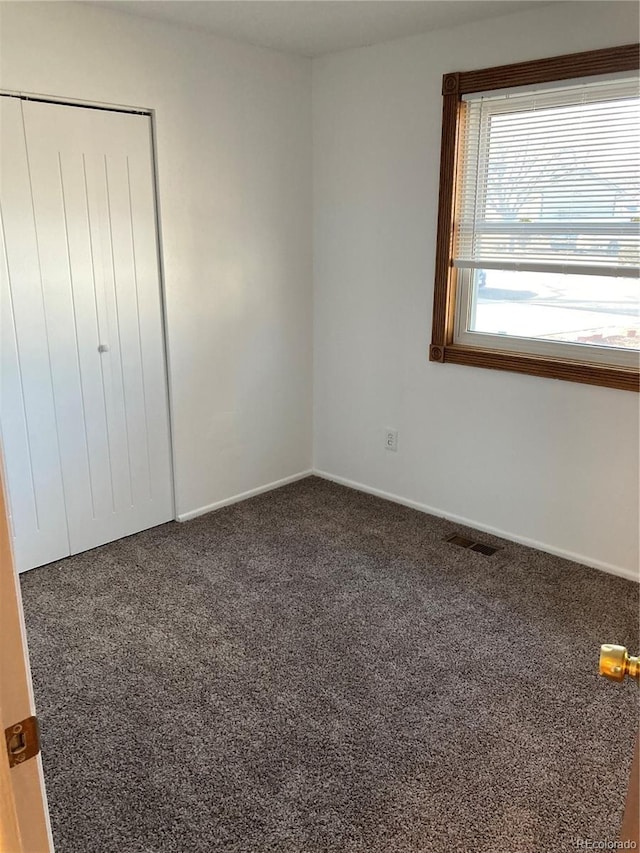 unfurnished bedroom with visible vents, dark colored carpet, and a closet