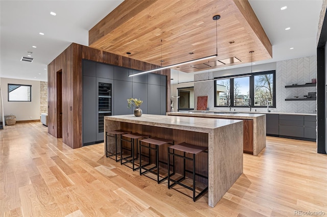 kitchen featuring a spacious island, tasteful backsplash, decorative light fixtures, light hardwood / wood-style floors, and a kitchen bar