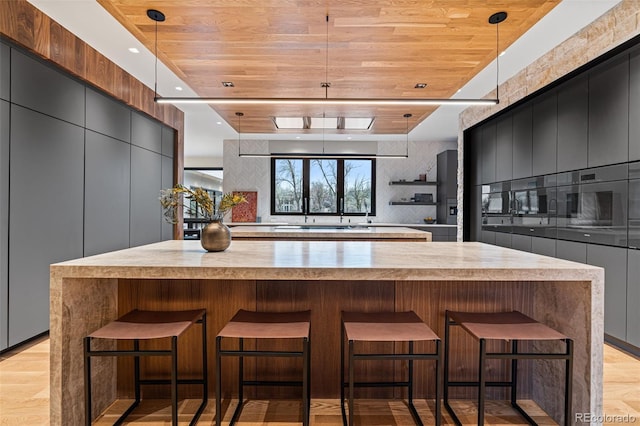 kitchen featuring pendant lighting, a large island, light hardwood / wood-style floors, and wood ceiling