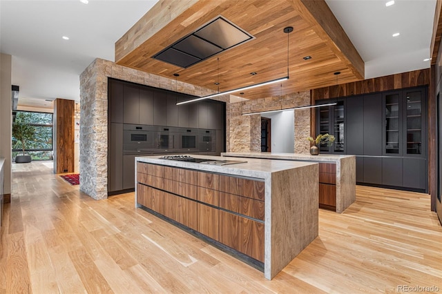 kitchen with pendant lighting, stainless steel gas stovetop, a spacious island, light wood-type flooring, and light stone countertops