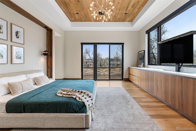 bedroom with access to exterior, multiple windows, a tray ceiling, and light hardwood / wood-style flooring