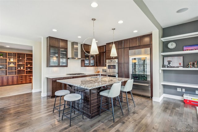 9244 E 37th Ave, Denver, CO 80238 - kitchen featuring wall chimney range hood, stainless steel appliances, dark brown cabinetry, a kitchen island with sink, and recessed lighting