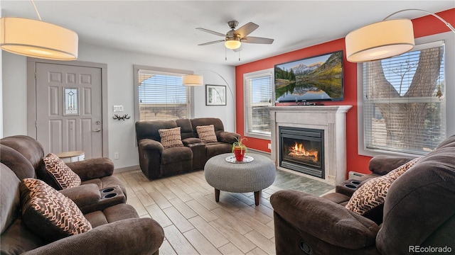 living room featuring a glass covered fireplace, wood finished floors, a ceiling fan, and baseboards