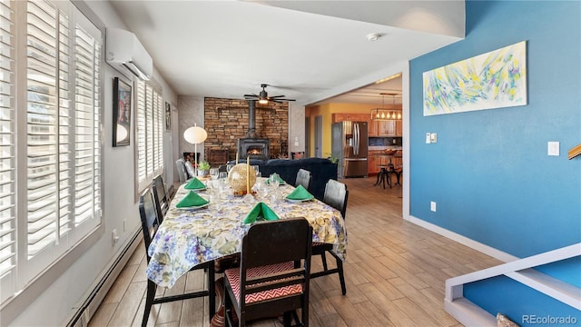 dining space featuring a baseboard radiator, wood finished floors, baseboards, an AC wall unit, and a wood stove