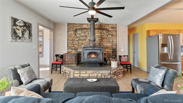 living room with ceiling fan, wood finished floors, a wood stove, and baseboards