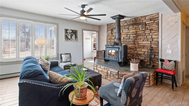 living room featuring baseboard heating, wood finished floors, a wood stove, and a ceiling fan