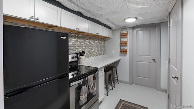 kitchen with electric range, white cabinets, light countertops, backsplash, and freestanding refrigerator