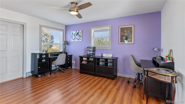 home office featuring a healthy amount of sunlight, a ceiling fan, baseboards, and wood finished floors