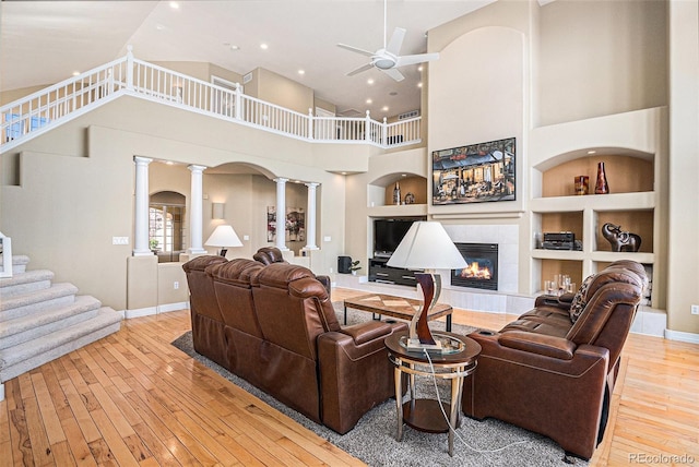 11065 W Rockland Dr, Littleton, CO 80127 - living room featuring ornate columns, hardwood / wood-style floors, ceiling fan, a tiled fireplace, and built in shelves