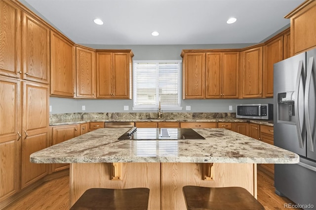 kitchen featuring light wood-style floors, a sink, appliances with stainless steel finishes, and a kitchen breakfast bar