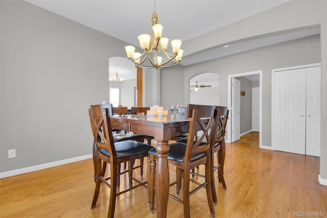 dining area with arched walkways, baseboards, light wood-style flooring, and ceiling fan with notable chandelier