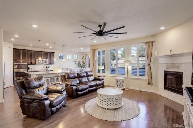 living room featuring a fireplace, hardwood / wood-style floors, a textured ceiling, and ceiling fan