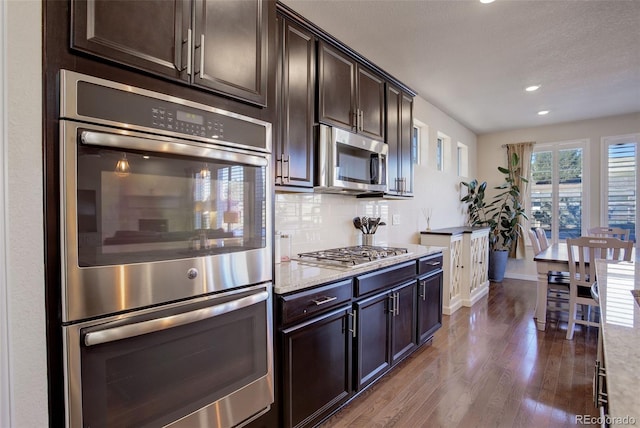 kitchen featuring light stone counters, appliances with stainless steel finishes, tasteful backsplash, dark brown cabinets, and dark hardwood / wood-style flooring