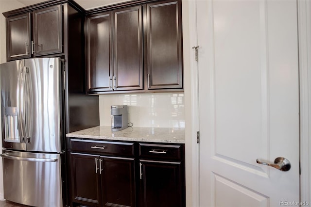 kitchen featuring tasteful backsplash, stainless steel fridge with ice dispenser, dark brown cabinets, and light stone countertops