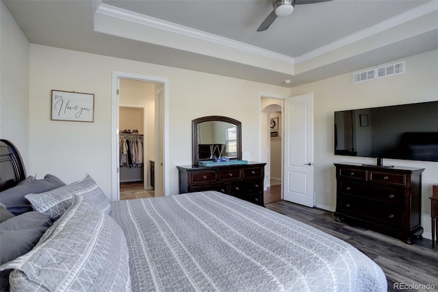 bedroom featuring a walk in closet, crown molding, ceiling fan, dark hardwood / wood-style floors, and a closet