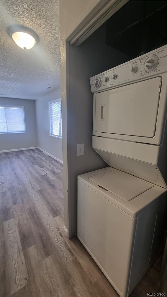 laundry area featuring stacked washer / drying machine, a textured ceiling, and light wood-type flooring