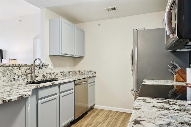 kitchen with light stone countertops, stainless steel appliances, light hardwood / wood-style floors, and sink