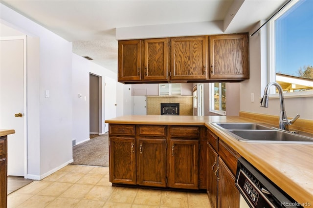 kitchen featuring sink, light carpet, dishwasher, kitchen peninsula, and a fireplace