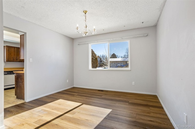 unfurnished dining area featuring an inviting chandelier, a textured ceiling, and dark hardwood / wood-style flooring