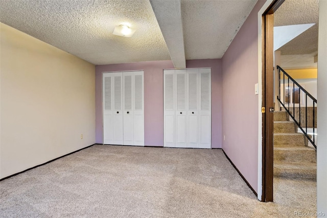 unfurnished bedroom with beamed ceiling, carpet flooring, two closets, and a textured ceiling