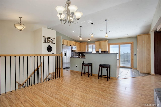 kitchen with light brown cabinetry, backsplash, hanging light fixtures, stainless steel appliances, and light hardwood / wood-style flooring