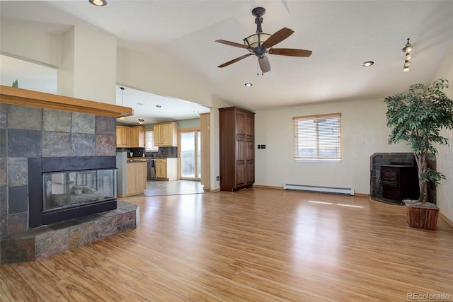 unfurnished living room with lofted ceiling, a tiled fireplace, baseboard heating, light wood-type flooring, and ceiling fan