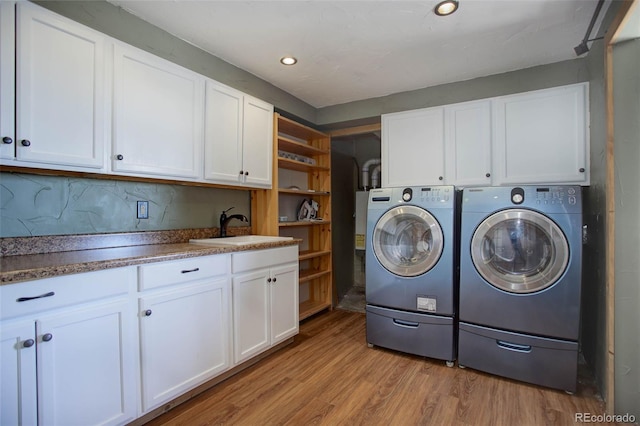 laundry area featuring washer and dryer, cabinets, sink, and light wood-type flooring