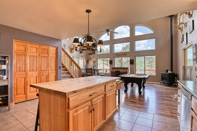 kitchen featuring a wood stove, stainless steel dishwasher, butcher block countertops, decorative light fixtures, and light tile patterned flooring