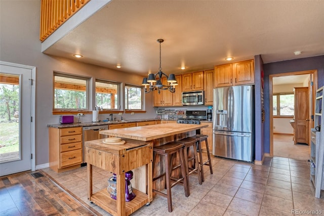 kitchen with a center island, hanging light fixtures, appliances with stainless steel finishes, butcher block countertops, and a chandelier