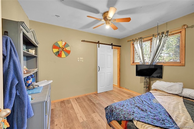 bedroom with ceiling fan, light hardwood / wood-style flooring, and a barn door